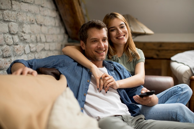 Lächelnde junge Paare, die sich zu Hause entspannen und fernsehen