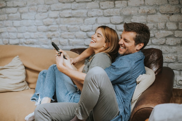 Lächelnde junge Paare, die sich zu Hause entspannen und fernsehen