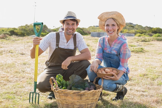 Lächelnde junge Paare mit Gemüse auf dem Gebiet