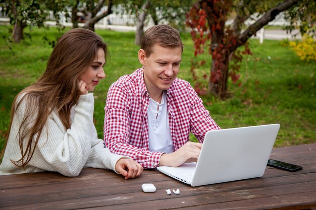 Lächelnde junge Paare verbringen Zeit zusammen im Park, lernen und arbeiten im Sitzen