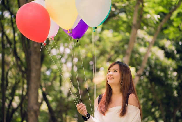 Lächelnde junge schöne asiatische Frauen mit langen braunen Haaren im Park. Mit regenbogenfarbenen Luftballons in ihren Händen.sunny und positive Energie der Natur.