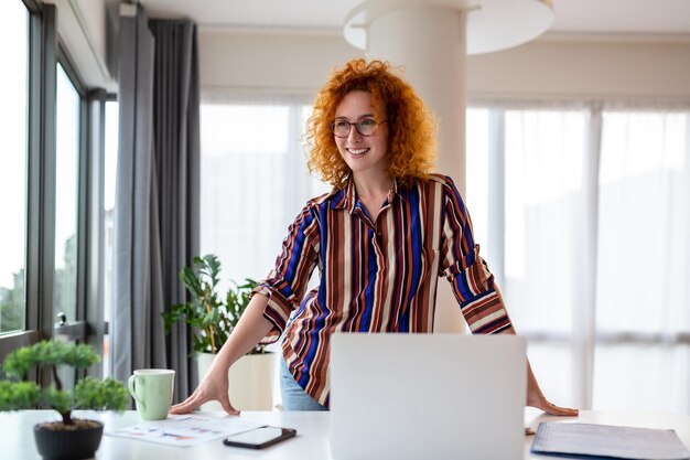 Lächelnde junge weibliche Angestellte stehen am Schreibtisch im Büro und schauen in die Ferne, denken oder visualisieren den beruflichen Erfolg. Glückliche Geschäftsfrau plant oder träumt am Arbeitsplatz Business-Vision-Konzept