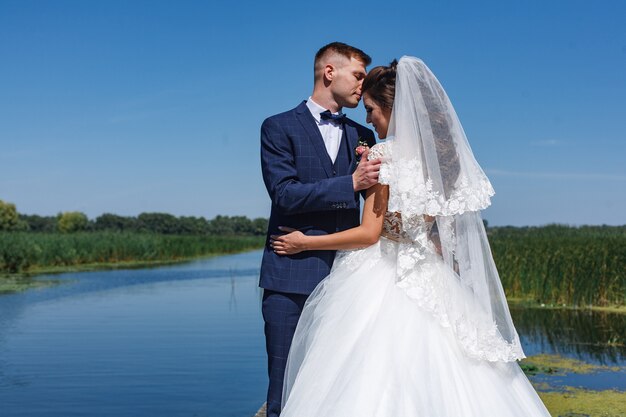 lächelnde Jungvermählten schauen sich sanft an und umarmen sich. Porträt ein Hochzeitspaar, das nahe Fluss aufwirft.