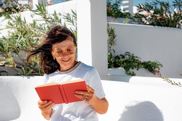 Lächelnde kaukasische ältere Frau entspannte das Sitzen auf einer Bank und las ein Buch, während sie die Freizeit genoss