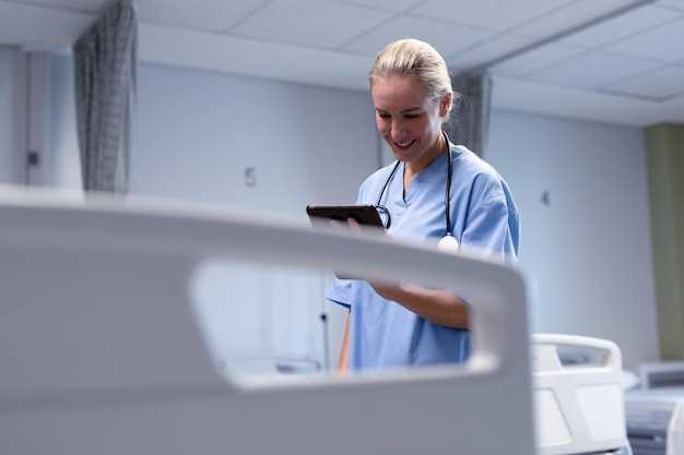 Foto lächelnde kaukasische ärztin im krankenhaus mit peelings und stethoskop mit tablet