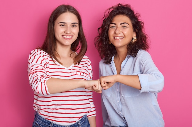 Lächelnde kaukasische Frauen Faust stoßen, zwei Freunde begrüßen oder unterstützen Teammotivation, Frauen tragen Freizeithemden