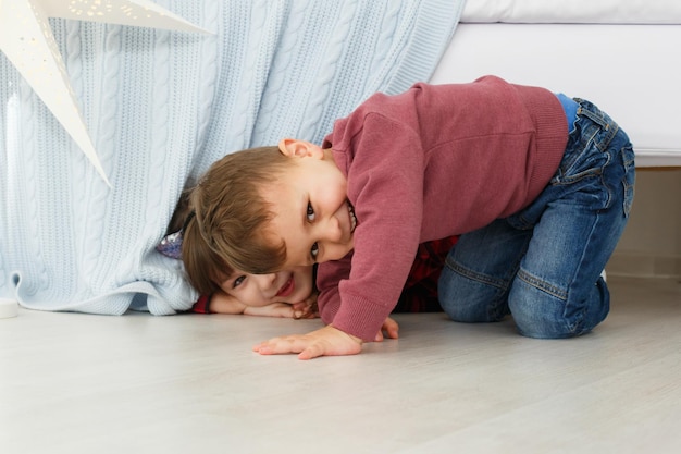 Lächelnde Kinder, die drinnen spielen Junge und Mädchen, die sich unter dem Bett verstecken Glückliches Kinderkonzept