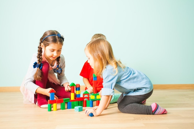 Lächelnde Kinder, die in der Vorschule spielen, bauen verschiedene Türme und Häuser aus bunten Holzklötzen. Kinder verbringen ihre Zeit damit, ihre Fantasie zu erschaffen und zu entwickeln