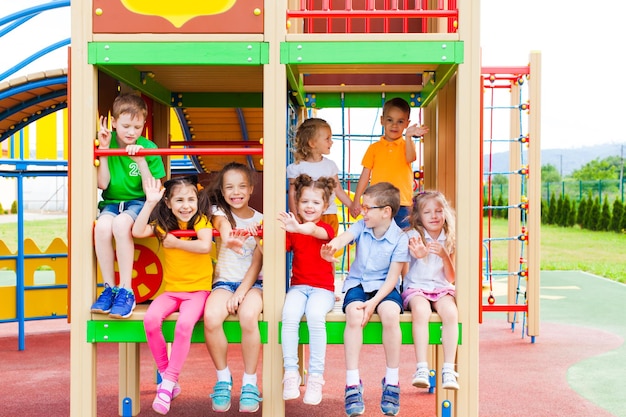 Lächelnde Kinder in bunten T-Shirts, die sich nach Spielen im Freien im Sommercamp ausruhen und auf einem Teil des Spielplatzes im Freien sitzen