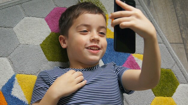 Foto lächelnde kinderjungenhand, die handy oder smartphone hält und selfie-porträtfoto oder videoanrufkonferenz macht