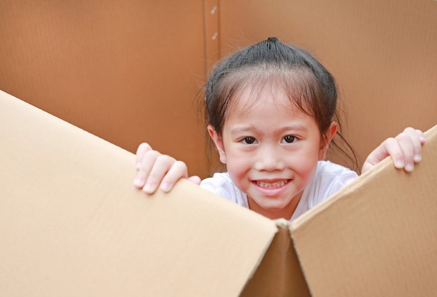 Lächelnde kleine asiatische Kindermädchenlüge in der großen Pappschachtel.