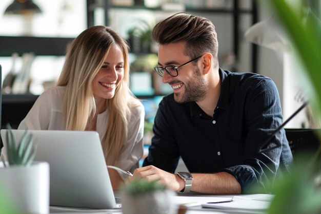 Lächelnde Kollegen besprechen ein Projekt, während sie mit einem Laptop in einem Büro im Innenraum arbeiten Teamwork im Unternehmen