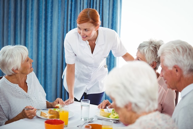 Lächelnde Krankenschwester, die ältere Person während des Frühstücks betrachtet