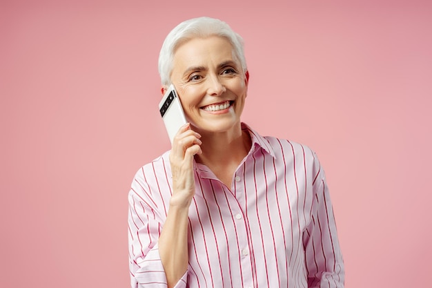 Lächelnde leitende Unternehmerin, die über ein Mobiltelefon spricht, isoliert rosa Studiohintergrund Porträt eines modernen Freelancers, der ein Smartphone anruft