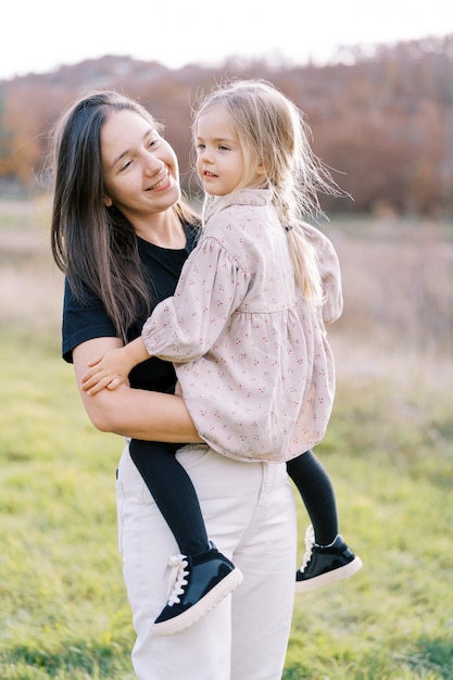 Foto lächelnde mutter blickt auf das kleine mädchen, das in ihren armen sitzt, während es auf dem rasen steht