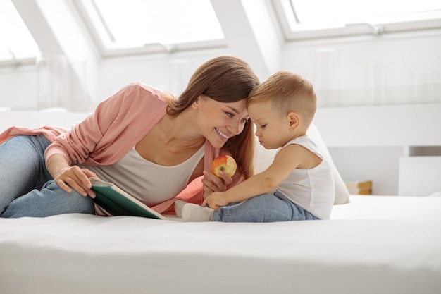 Lächelnde Mutter, die ein Buch für ihren kleinen Sohn im Bett liest