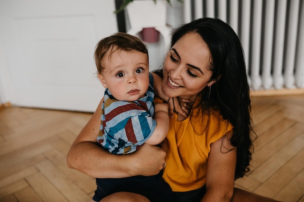 Lächelnde Mutter mit Baby, der auf dem Holzboden sitzt