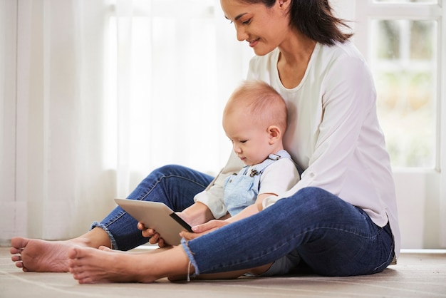 Lächelnde Mutter und Baby sitzen auf dem Boden und spielen auf einem Tablet-Computer