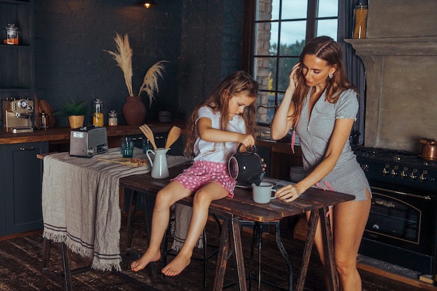 Lächelnde Mutter und Kind Tochter Mädchen kochen und Spaß in der dunklen Küche zu Hause haben.