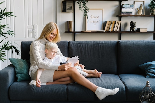 Lächelnde Mutter und Sohn schauen sich Fotos an, während sie sich auf der Couch im Wohnzimmer ausruhen