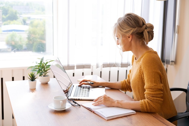 Lächelnde nette kaukasische Geschäftsfrau, die an ihrem Schreibtisch an einem Laptop arbeitet