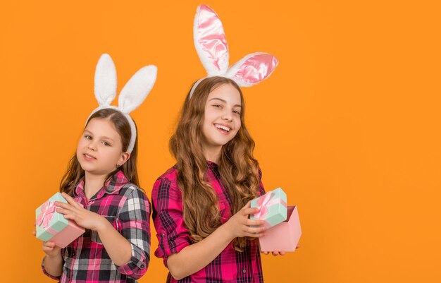 Foto lächelnde osterkinder in hasenohren halten eine geschenkkiste auf gelbem hintergrund mit kopierraum