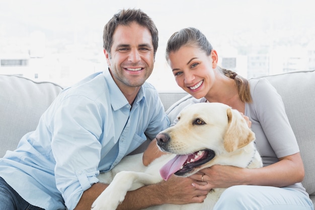 Lächelnde Paare, die ihr gelbes Labrador auf der Couch streicheln