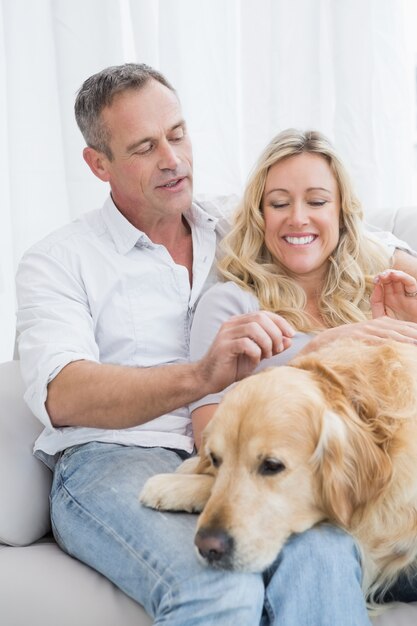 Lächelnde Paare, die ihren goldenen Apportierhund auf der Couch streicheln