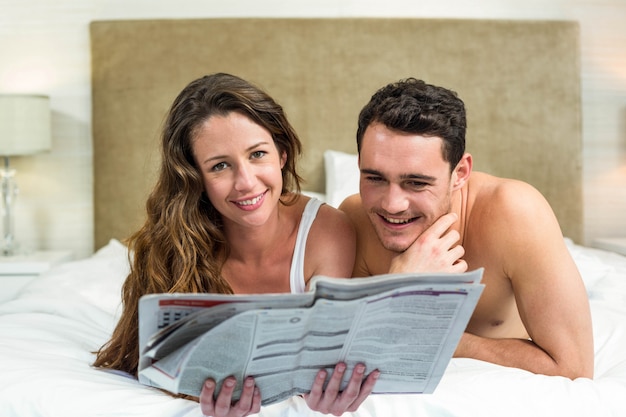 Lächelnde Paare, die im Bett mit einer Zeitung liegen