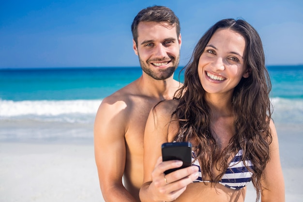 Lächelnde Paare unter Verwendung des Smartphone am Strand