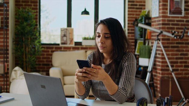 Lächelnde Person, die Handy-Benachrichtigungen am Computertisch überprüft