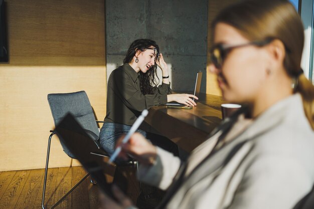 Lächelnde, positive, vielfältige Kollegen in Freizeitkleidung, die an einem neuen Projekt arbeiten, sitzen während eines Meetings in einem hellen, kreativen Arbeitsbereich am Verhandlungstisch zusammen