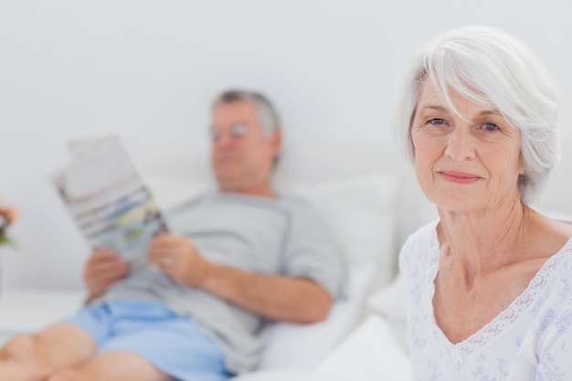 Lächelnde reife Frau, die im Bett sitzt