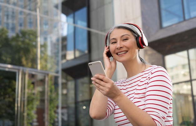 Lächelnde reife Frau mit drahtlosem Kopfhörer, die Musik auf der Straße hört