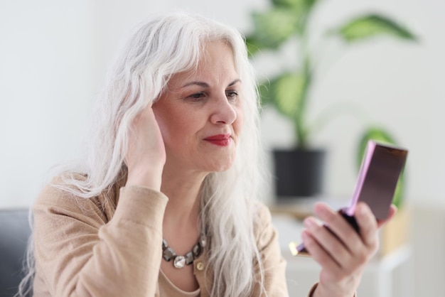 Lächelnde reife Frau mit langen grauen Haaren untersucht Gesicht