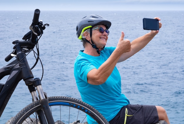 Lächelnde reife Radfahrerin, die mit ihrem Elektrofahrrad gesunde Aktivitäten auf See genießt