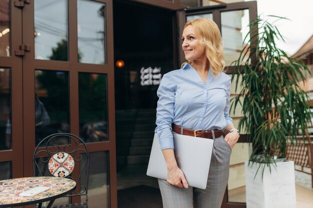 Lächelnde reife Unternehmerin, die Laptop gegen Caffe hält Erfolgreiche Frau Office Worker-Konzept