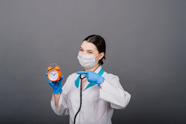 Lächelnde Ärztin in der Maske, die auf Uhr zeigt, Zeit zum Impfstoff