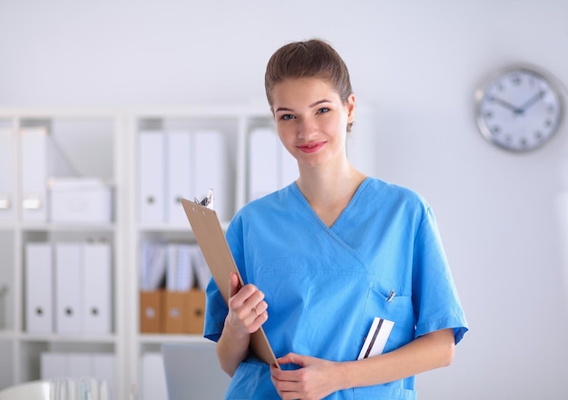 Lächelnde Ärztin mit einem Ordner in Uniform, die im Krankenhaus steht