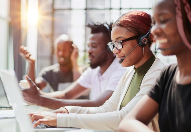 Lächelnde schöne Afroamerikanerfrau, die im Kundenkontaktcenter mit verschiedenem Team arbeitet