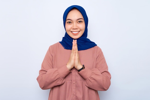 Lächelnde schöne asiatische muslimische Frau in Freizeithemd gestikuliert Eid Mubarak-Gruß isoliert über weißem Hintergrund Religiöses Lifestyle-Konzept der Menschen