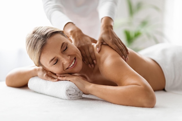 Foto lächelnde schöne frau erhält entspannende schultermassage im spa-salon