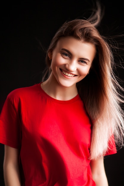 Lächelnde schöne junge Frau im roten T-Shirt und in Jaens, die mit den Händen auf Hüfte aufwerfen