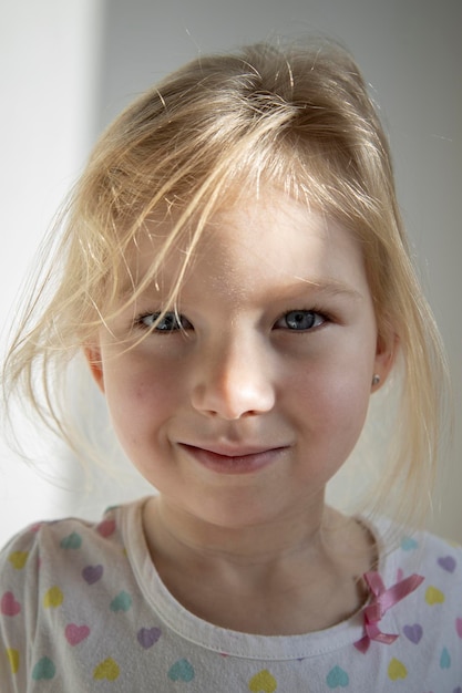 Foto lächelnde schöne kindermädchenblondine unter natürlichem licht auf dem hintergrund einer weißen wand