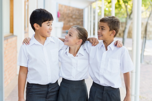 Lächelnde Schulkinder, die mit dem Arm herum im Korridor stehen