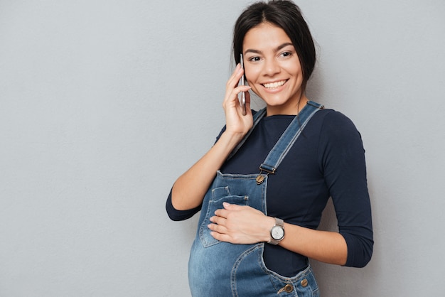 Lächelnde schwangere Dame, die per Telefon spricht.