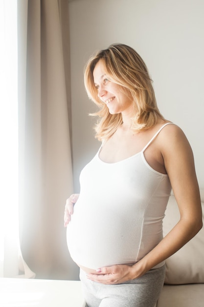 Lächelnde schwangere Frau, die aus dem Fenster schaut. Konzept - Erwartungen für Baby
