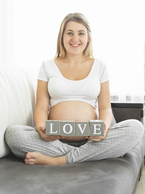 Lächelnde schwangere Frau, die Blöcke mit Buchstaben hält, die Wort Liebe machen