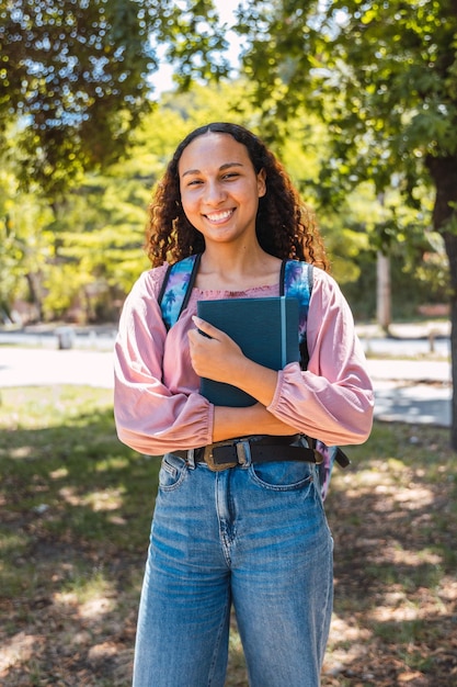 Lächelnde schwarze Studentin, die Bücher im Park hält. Gesundes Selbstbewusstsein Centennial Generation