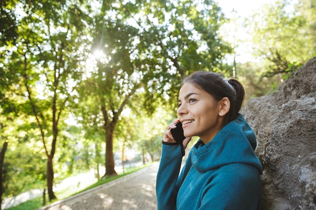 Lächelnde Sportlerin, die auf Handy spricht, während sie draußen im Park steht